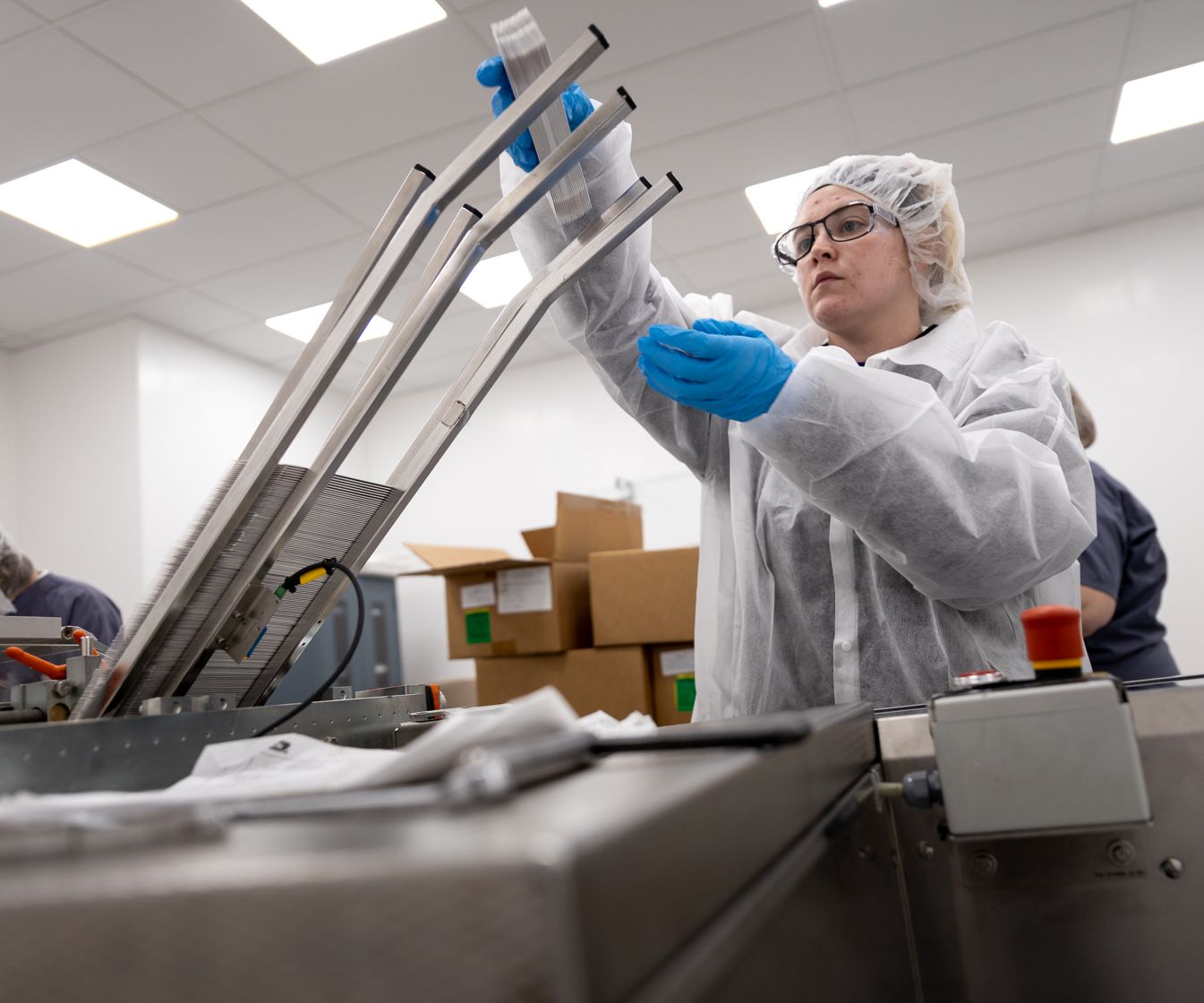 Woman with white gown and hairnet loading a packaging machine.