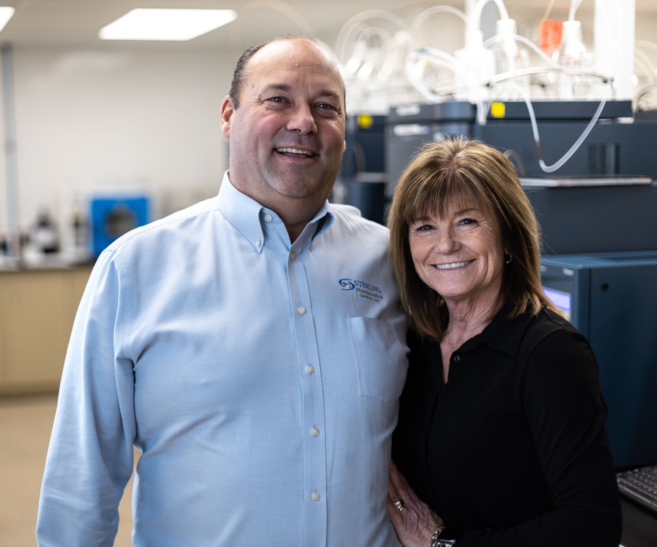 Husband and wife pictured smiling in a lab facing the camera.