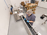 woman with blue gloves and hair net operating an assembly line for packaging goods